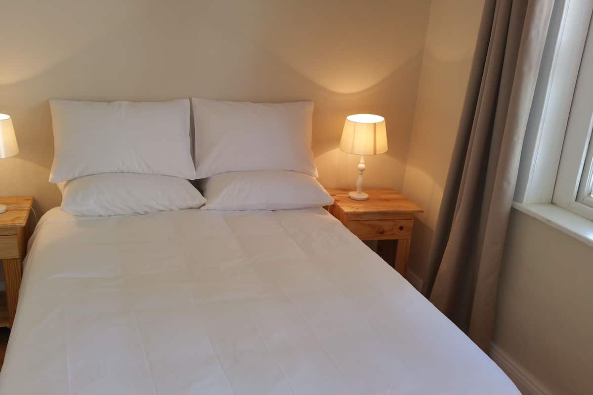 Een net opgemaakt bed met witte lakens en twee bedlampjes op houten nachtkastjes.