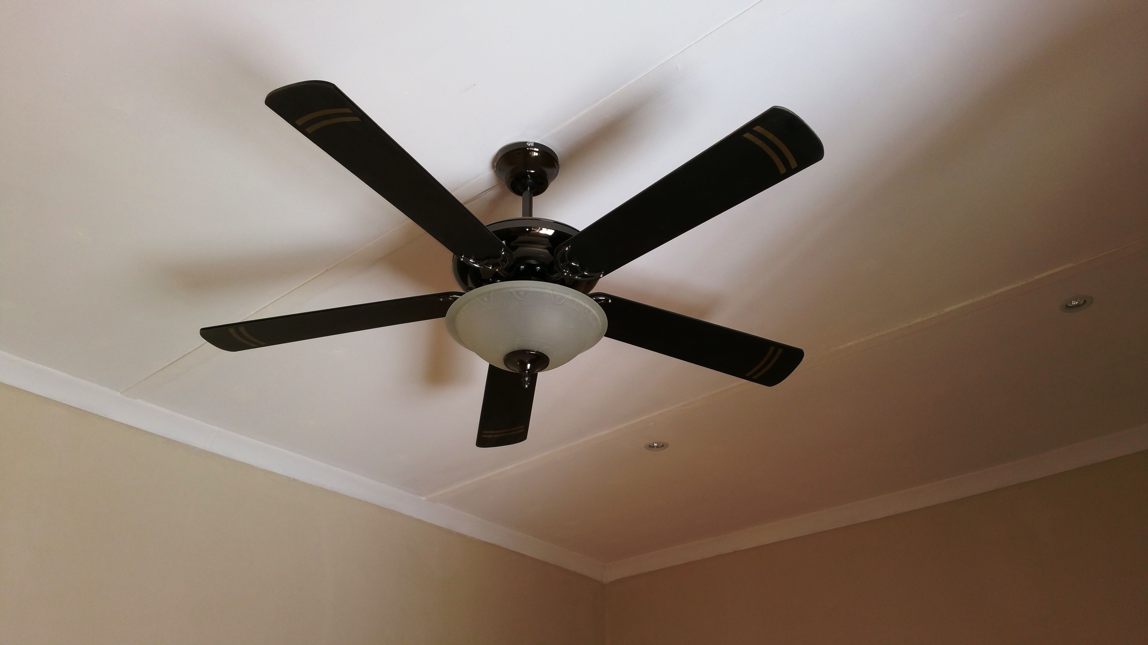 A ceiling fan with five blades and a central light fixture in a room with white walls and a white ceiling.