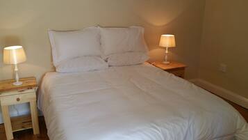 A neatly made bed with white bedding, two bedside lamps, and a wooden nightstand with a drawer.
