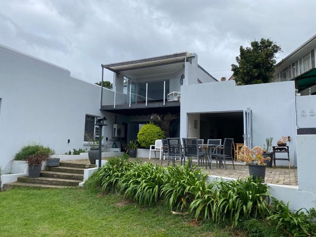 Un edificio moderno de dos pisos con un área de estar al aire libre cubierta y una escalera que lleva a la entrada.