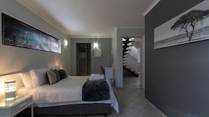 A modern bedroom with a bed, bedside table, and a painting on the wall. - Dockside Guest House (Port Alfred)