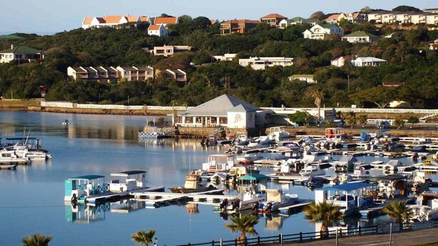 A marina with numerous boats docked, surrounded by residential buildings on a hillside. - Dockside Guest House (Port Alfred)