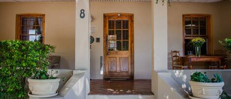 A house with a wooden door, a number '8' on the wall, and potted plants on the steps.