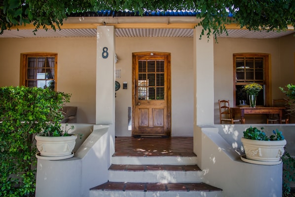 A house with a wooden door, a number '8' on the wall, and potted plants on the steps. - Guesthouse LaRachelle (Swellendam)