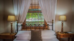 A neatly made bed with a single decorative pillow, flanked by two bedside tables with lamps, in a room with a window and curtains. - Guesthouse LaRachelle (Swellendam)