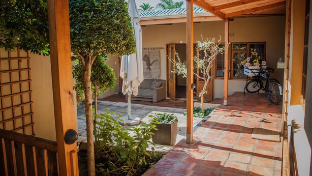 A covered patio area with a tiled floor, wooden beams, and potted plants. - Guesthouse LaRachelle (Swellendam)