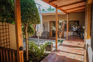 A covered patio area with a tiled floor, wooden beams, and potted plants. - Guesthouse LaRachelle (Swellendam)