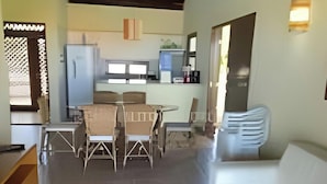Amplia sala de estar con una mesa de comedor y sillas, un sofá blanco y una cocina al fondo.