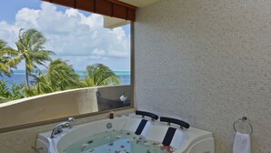 Un baño con una bañera grande, ventana con vistas al océano y un perchero para toallas.