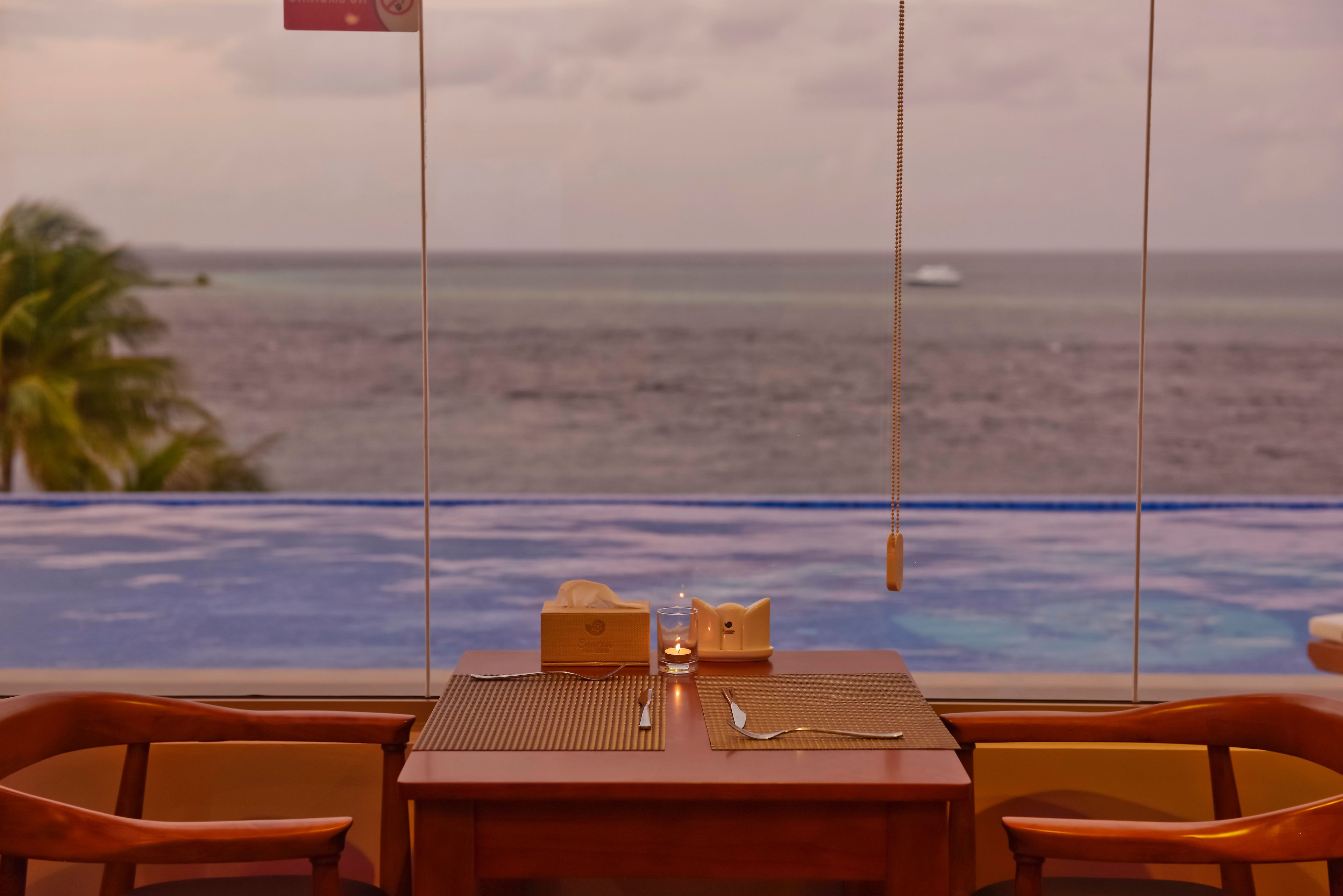 A dining table with a view of the ocean, a bottle of water, and a tissue box.