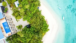 Vista aérea de un complejo turístico en la playa con piscina, palmeras y aguas turquesas cristalinas.