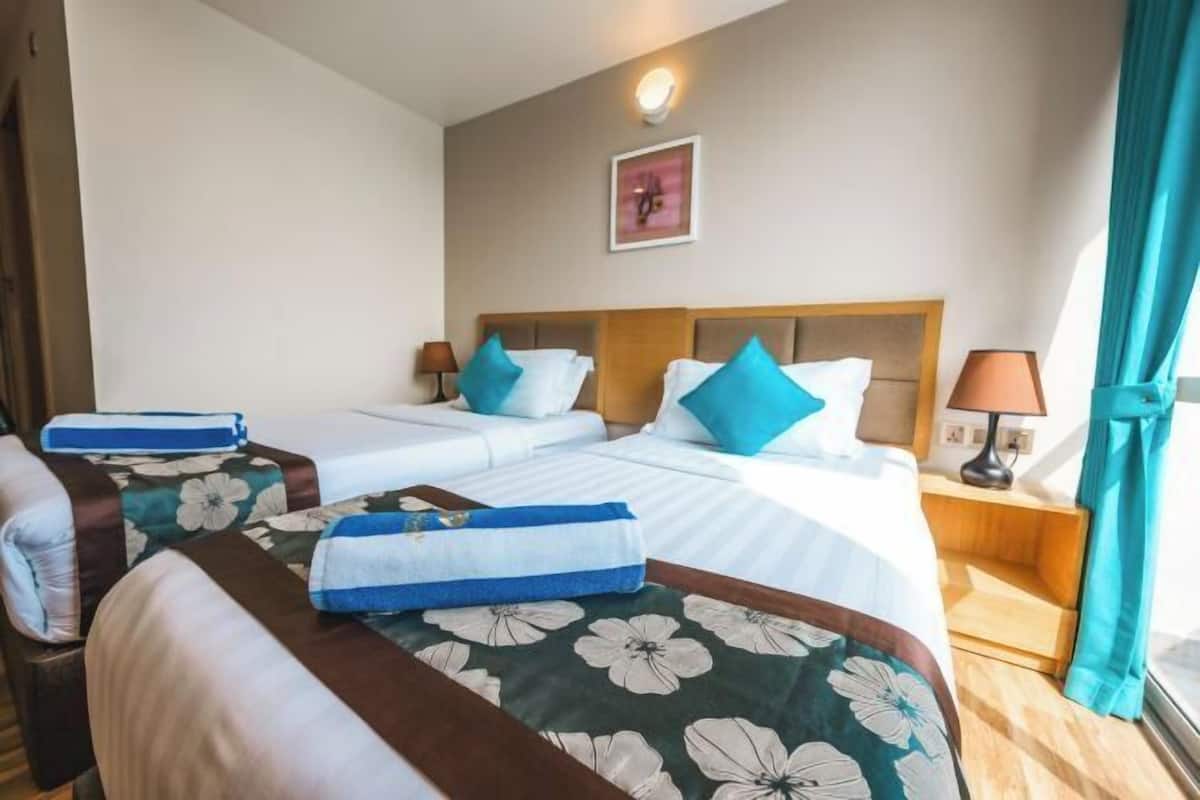 A hotel room with two beds, a wooden headboard, a nightstand with a lamp, and a window with curtains.