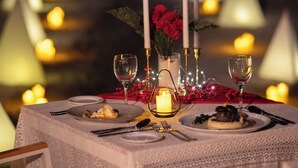 Una mesa dispuesta para comer con velas, un florero con flores y un centro de mesa con vela encendida.