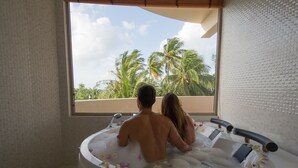 Una pareja en una bañera con vista a palmeras a través de una ventana.