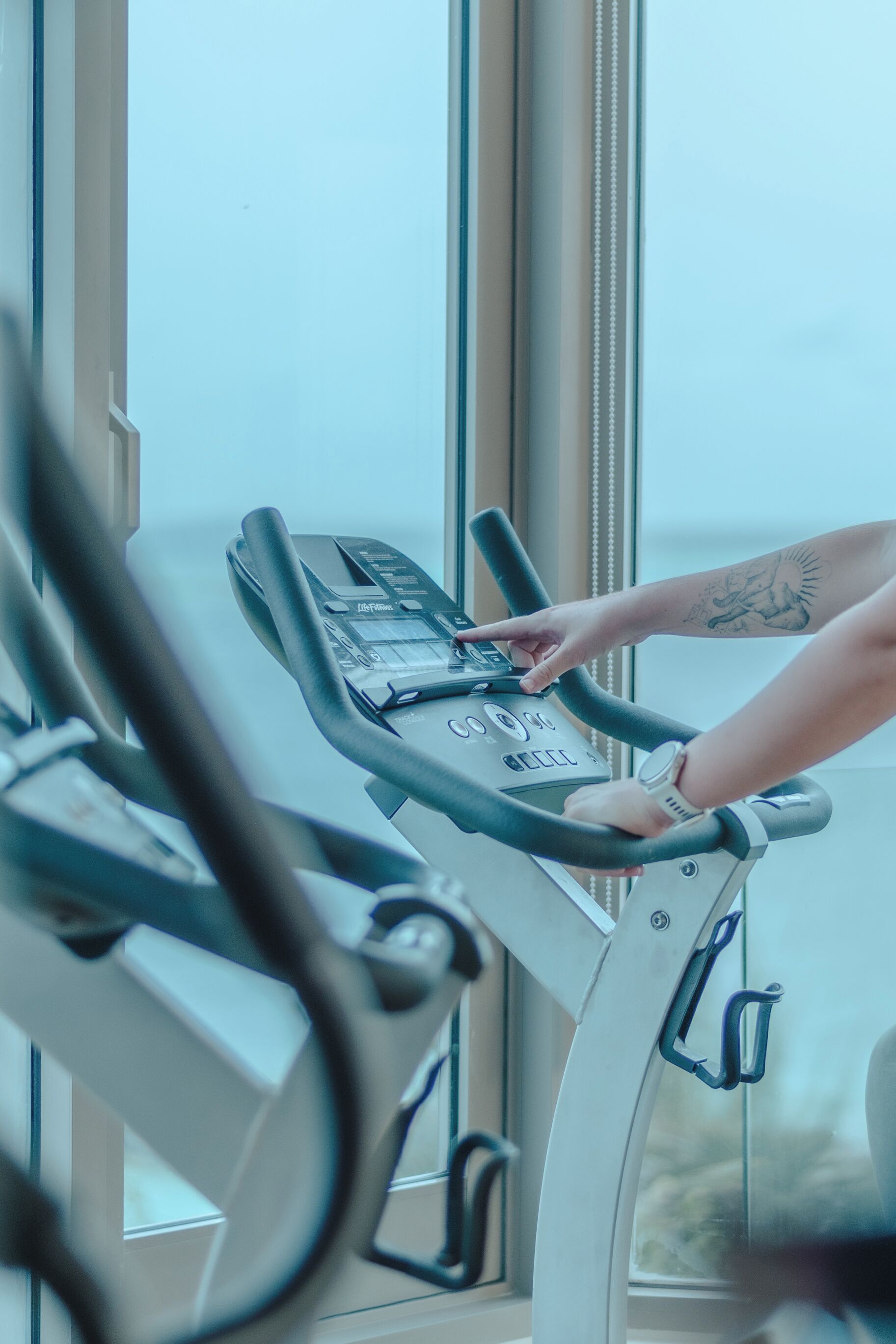 A person using a stationary bike in a gym with large windows and a clear view outside.
