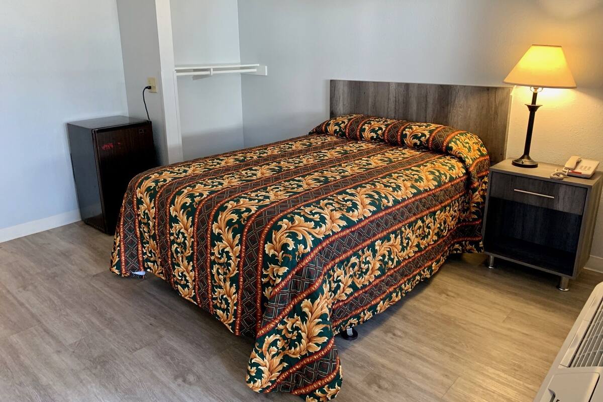 A neatly made bed with a patterned bedspread, a bedside table with a lamp, and a small cabinet.