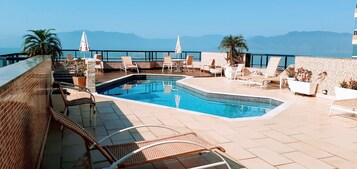 Una piscina al aire libre, sombrillas, sillones reclinables de piscina