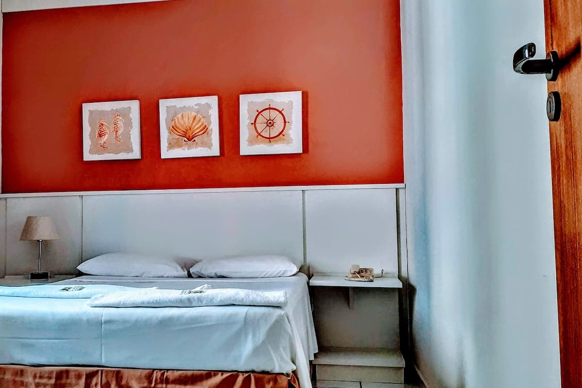 Habitación de hotel con cama, mesita de noche, lámpara y tres cuadros en la pared.