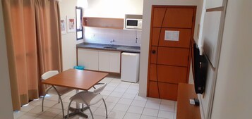 Cocina compacta con microondas, lavamanos y refrigerador pequeño. Hay una mesa con dos sillas y un bote de basura azul.