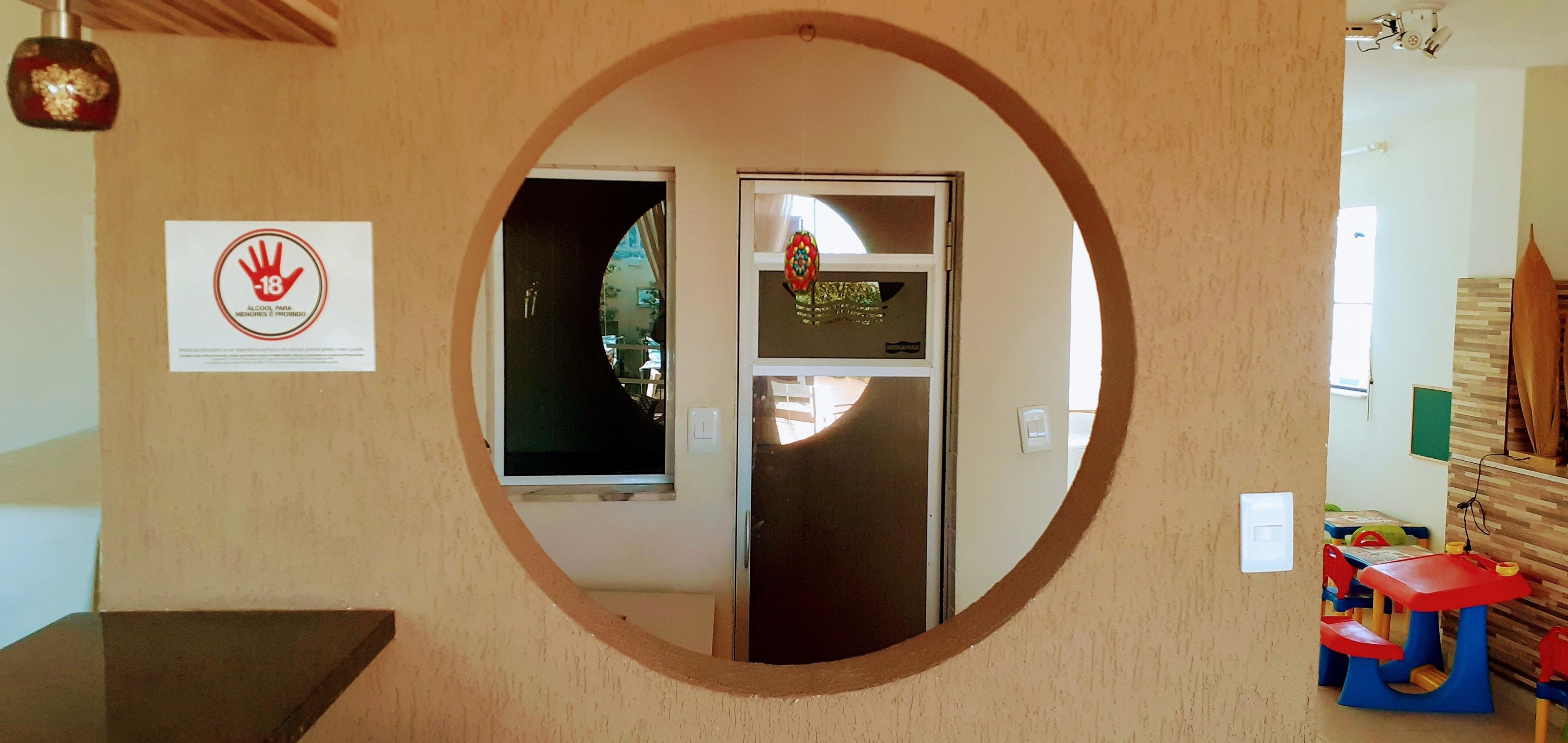 Uno specchio circolare che riflette una porta, un segnale con simbolo di mano e un'area giochi per bambini con giocattoli.