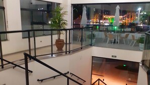 A multi-level interior with glass railings, a staircase, and a view of an outdoor area with a carousel. - Jangada Flat Service (Caraguatatuba)