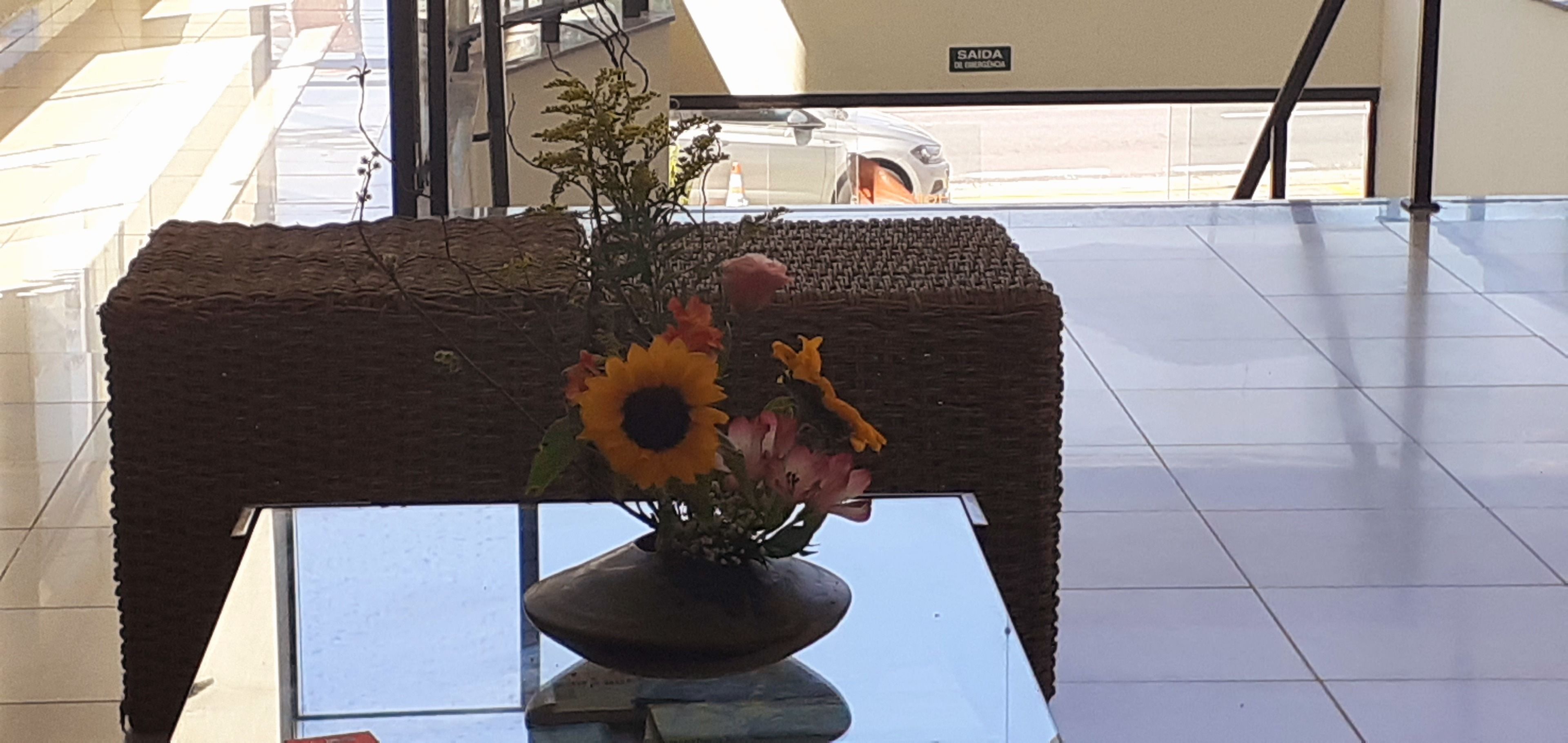 A glass table with a vase of sunflowers and pink flowers.