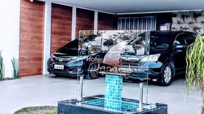 A modern hotel entrance with a blue-tiled column, two parked cars, and a building with a red facade. - Jangada Flat Service (Caraguatatuba)