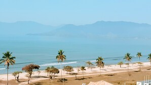 A beach with palm trees and mountains in the background. - Jangada Flat Service (Caraguatatuba)