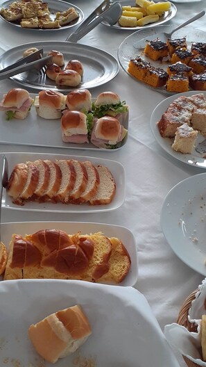 A buffet table with various food items including sandwiches, pastries, and a sliced loaf of bread. - Jangada Flat Service (Caraguatatuba)