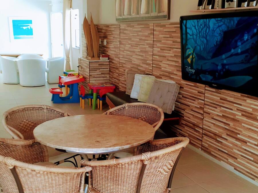 A dining area with wicker chairs and a round table, a television mounted on the wall, and a wooden wall with a patterned design.