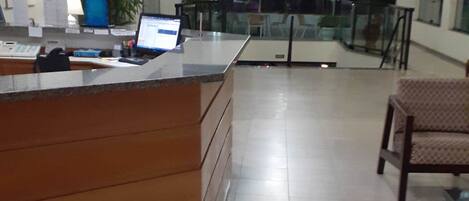 Amplia recepción con mostrador de madera, una computadora portátil y una planta en maceta.
