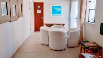 Un pasillo con una puerta de madera, una pequeña mesa con sillas y un ventanal con vistas al mar.