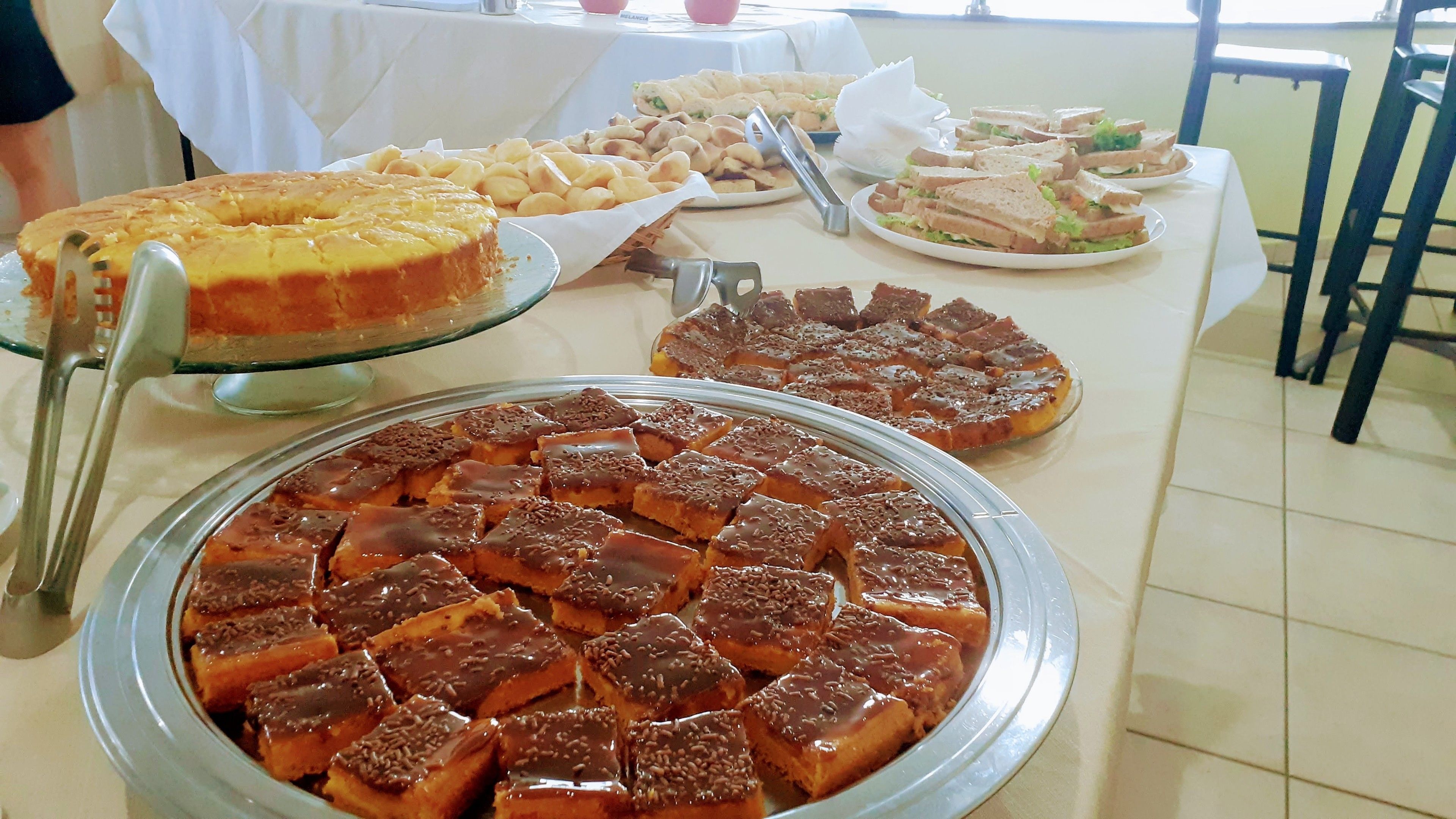 A buffet table with various desserts including a large cake, a tray of brownies, and sandwiches.