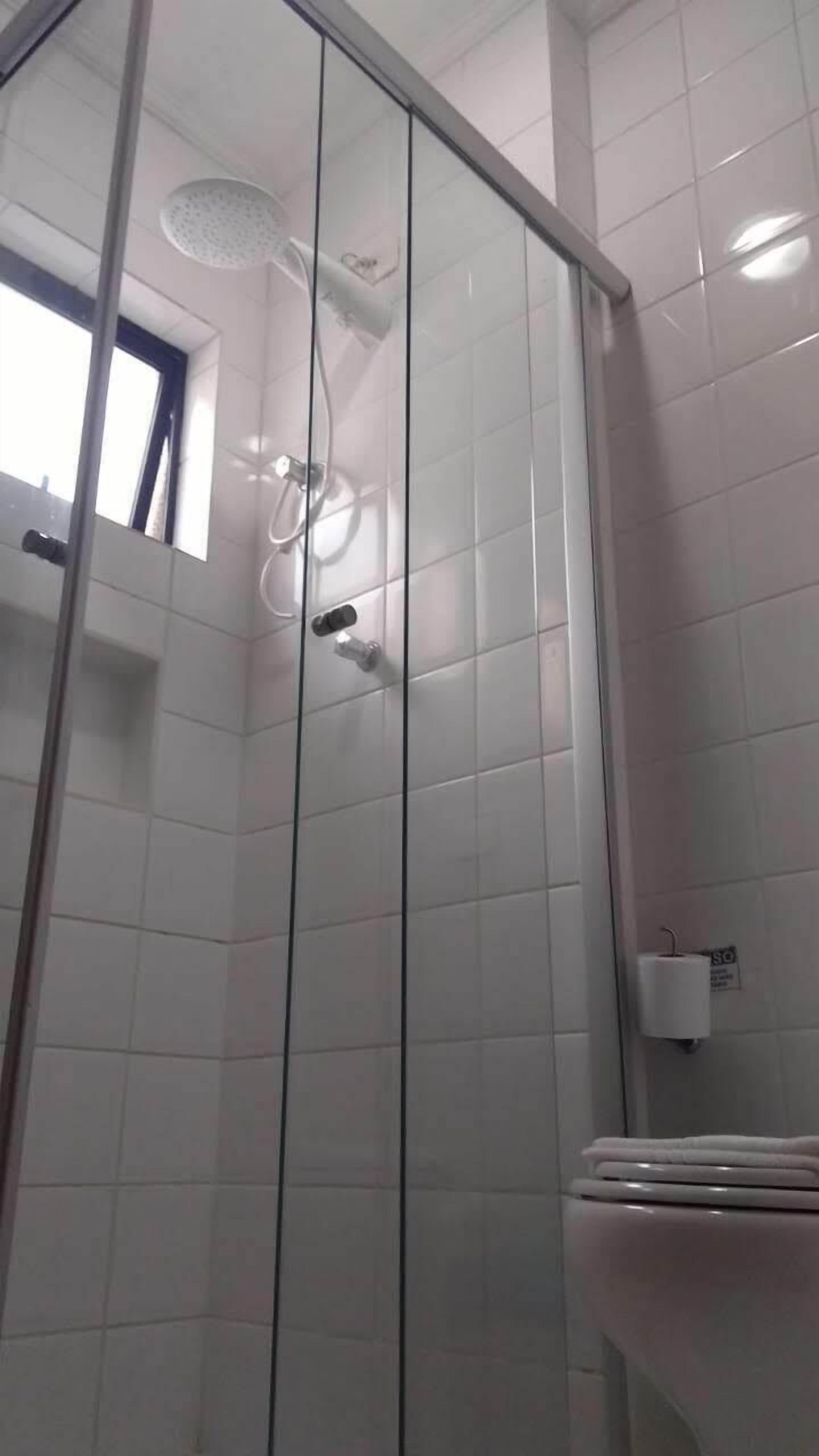 Une douche en verre avec un pommeau de douche à main, des toilettes et un distributeur de serviettes en papier fixé au mur.