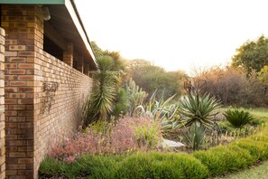 A brick building with a garden featuring various plants and a brick wall. - Woodlands Stop Over and Lodge (Francistown)