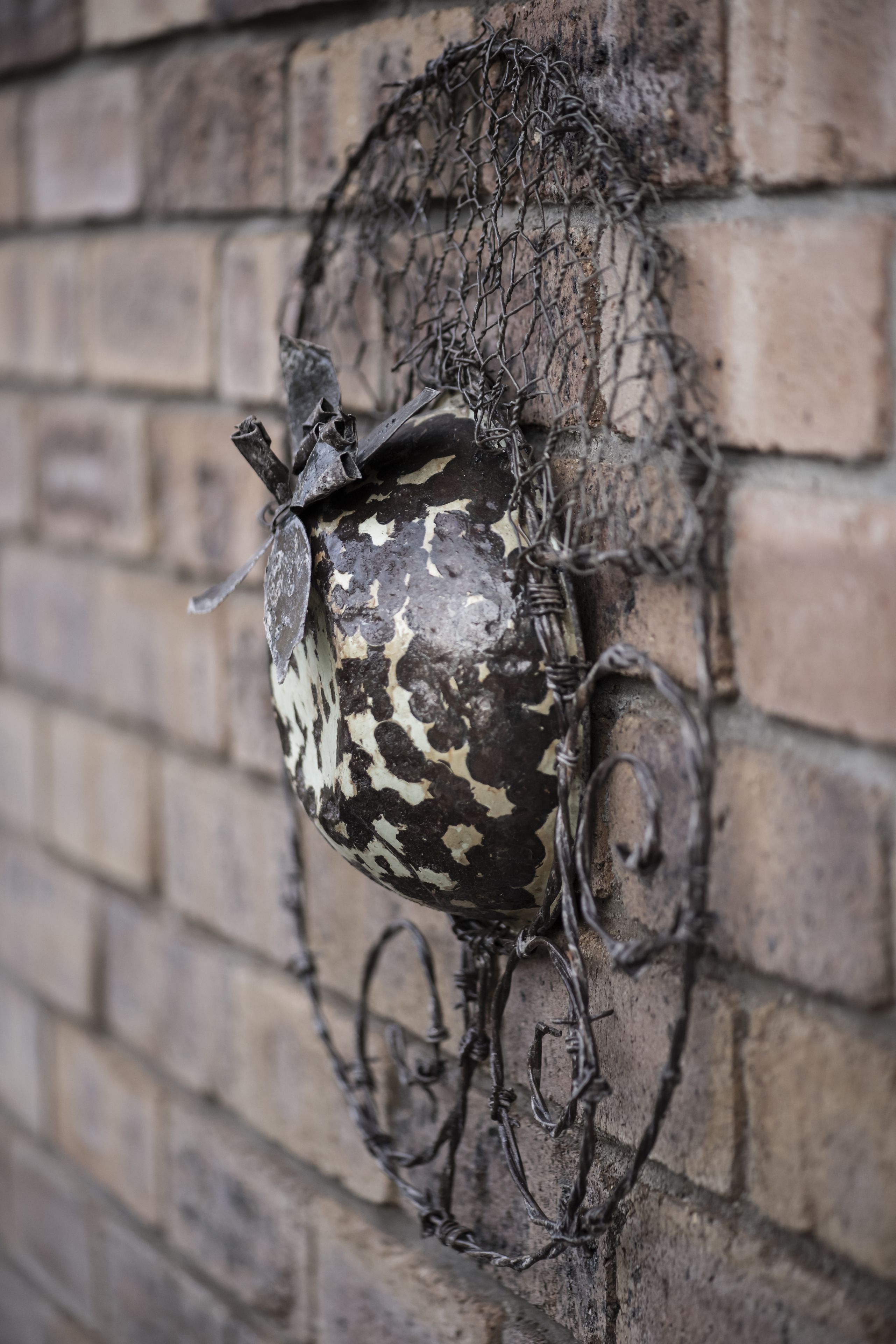 Una escultura de metal decorativa con superficie texturizada, fijada a una pared de ladrillo.