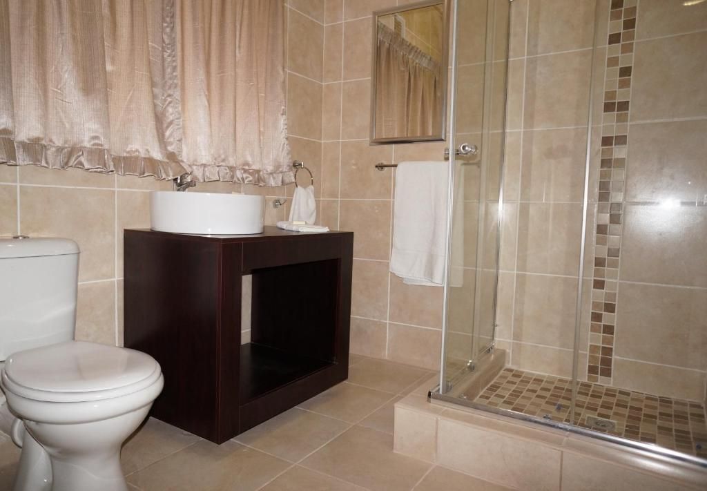 Un baño con inodoro, lavamanos, espejo y zona de ducha.