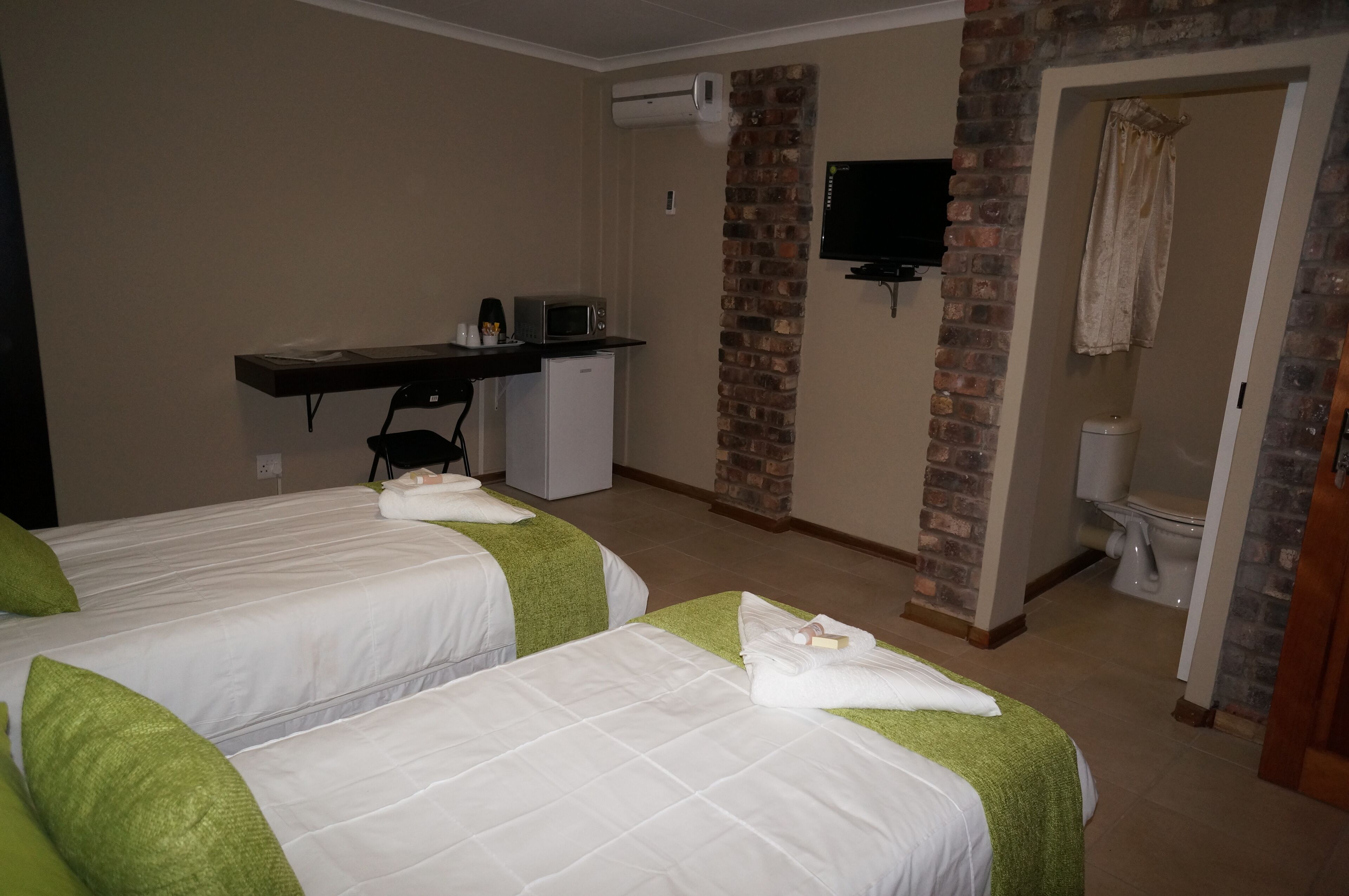 A hotel room with two beds, a desk with a computer and a small fridge, a TV mounted on the wall, and a bathroom with a toilet and shower.
