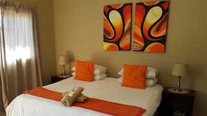 A hotel room with a large bed, two nightstands, a pair of lamps, and a window with curtains.