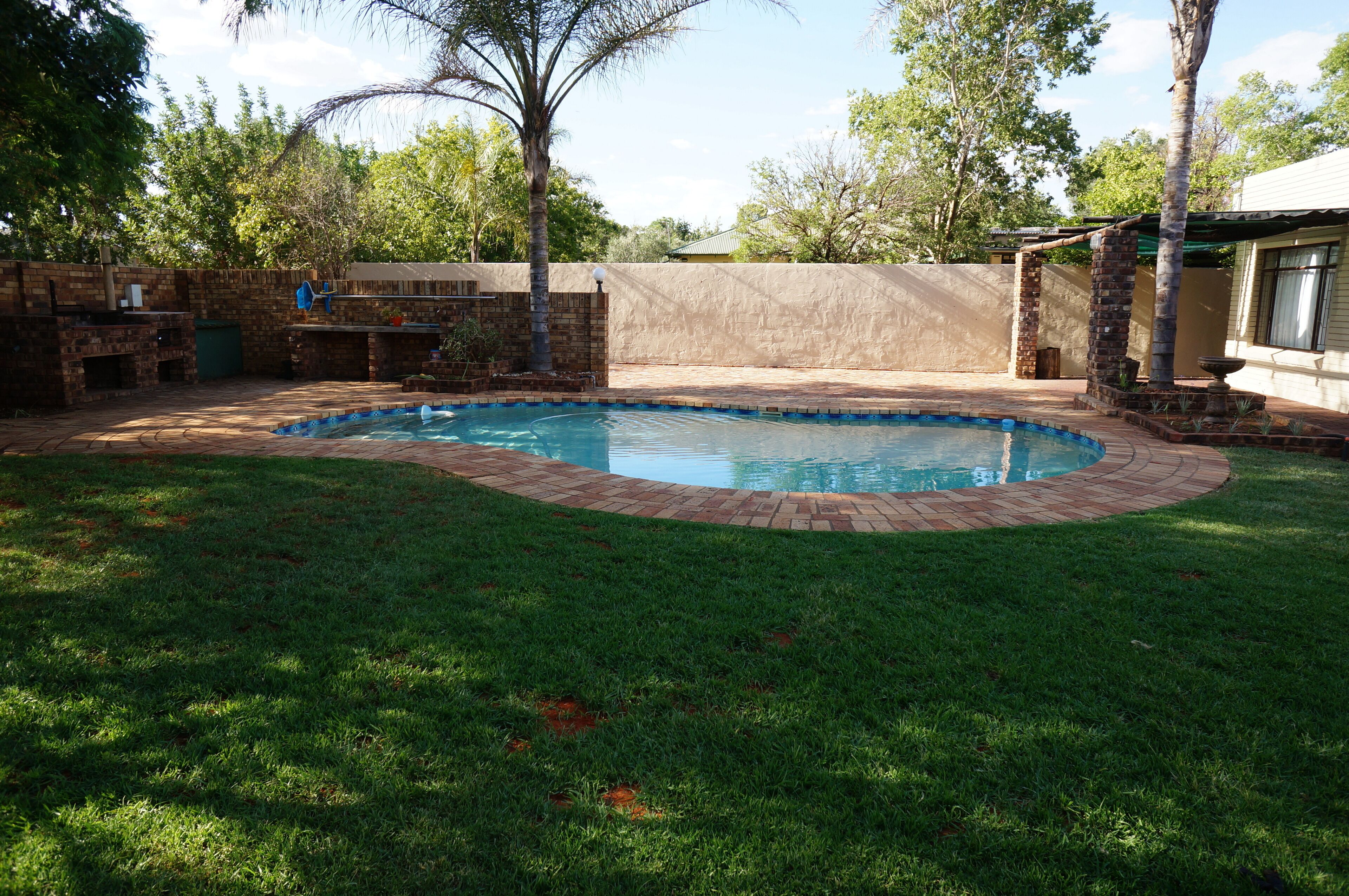Un jardin avec une piscine, une terrasse en briques et une pelouse verdoyante.
