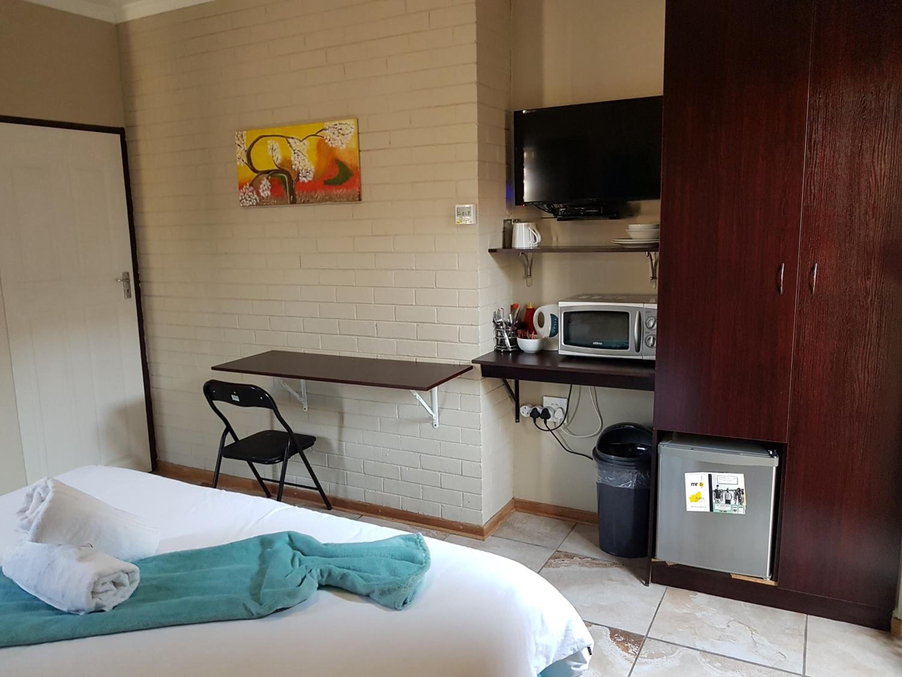 Habitación de hotel con cama, escritorio con silla, microondas, televisor y refrigerador.