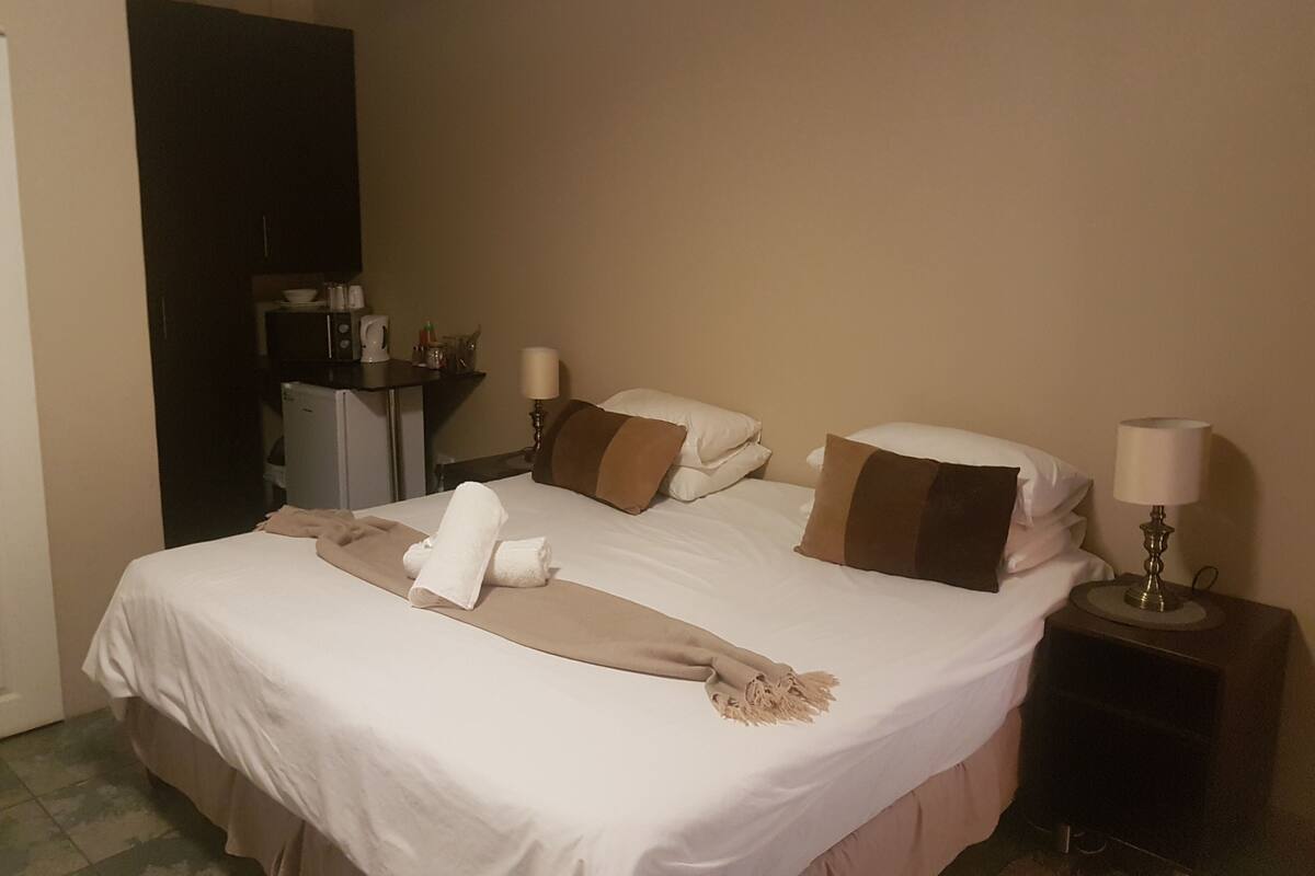 Ein Hotelzimmer mit einem Bett, Nachttischlampen, einem Schreibtisch und einem kleinen Kühlschrank.