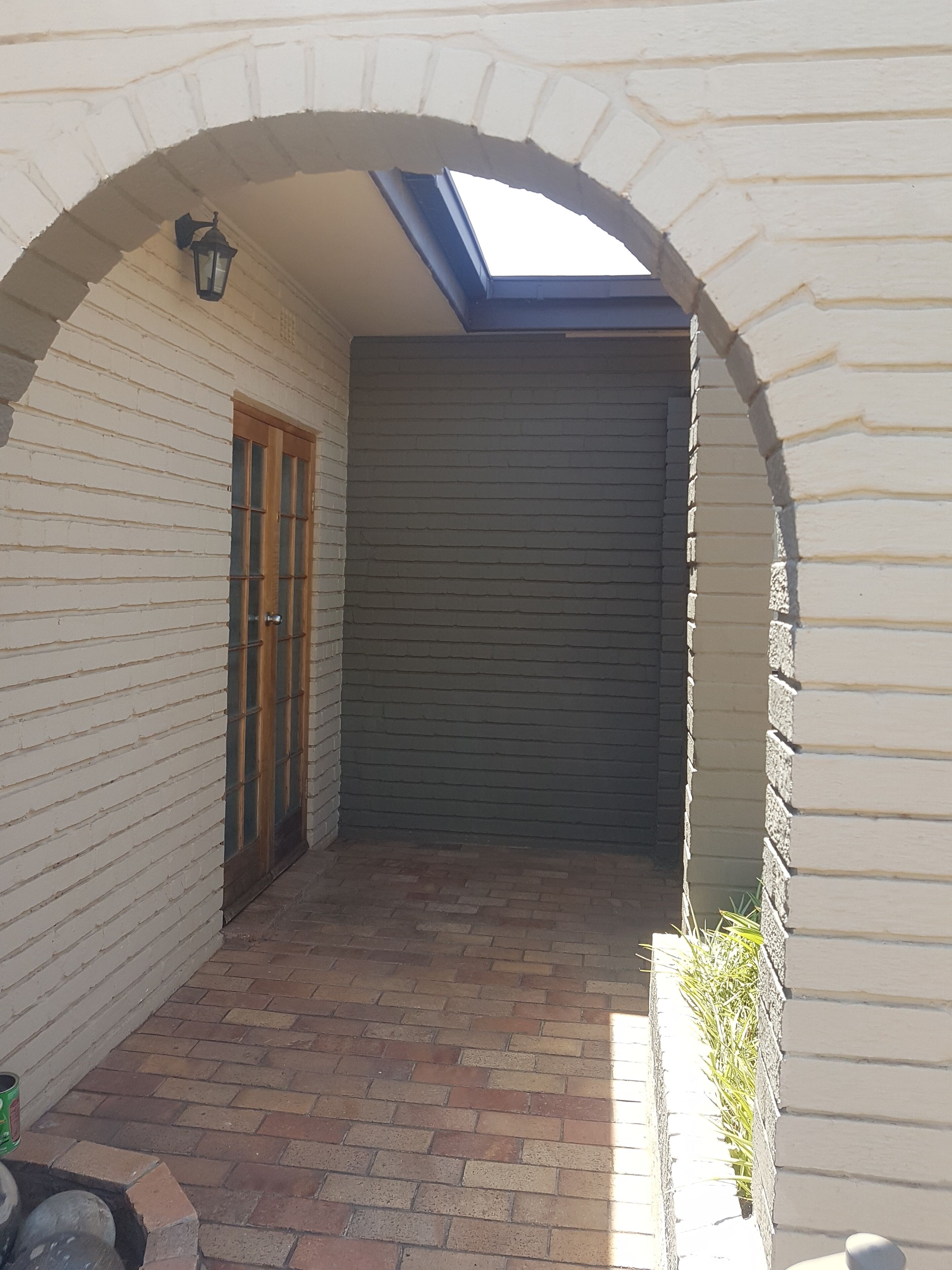 A covered patio area with a brick floor, a wooden door, and a closed garage door.