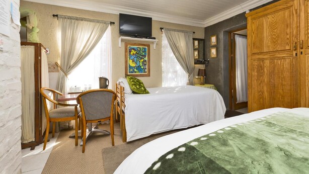 A bedroom with a bed, a desk with chairs, a TV, and a wardrobe. - Oceanview B&B 85 Oceanview Drive (Struisbaai)