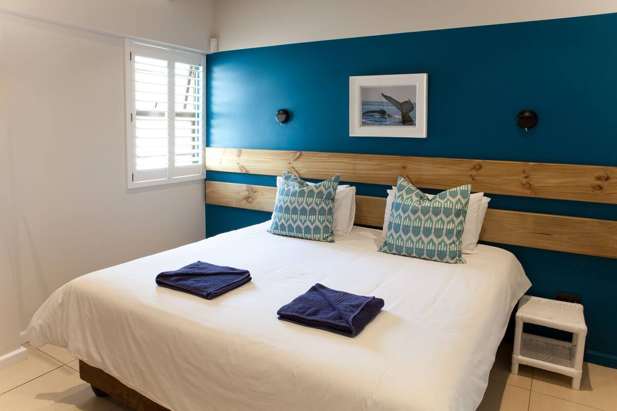 Quarto com uma cama grande, cabeceira com acabamento em madeira e parede azul decorativa.