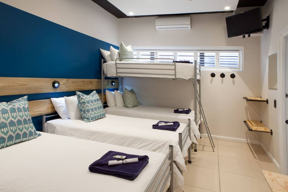Quarto de hotel com beliches, televisão na parede e janela com persianas.