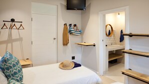 A bedroom with two beds, a TV, a bathroom with a sink and mirror, and a coat rack. - Plett Beachfront Accommodation (Plettenberg Bay)