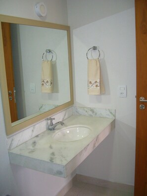 A bathroom with a marble sink, a mirror, and two towels hanging on hooks. - Apartamento Varandas da Praia (Porto Seguro)