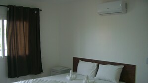 Une chambre d’hôtel avec un lit bien fait, une table de chevet, une commode et un appareil de climatisation fixé au mur.