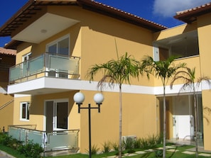 A two-story residential building with balconies, a small garden, and a clear sky.